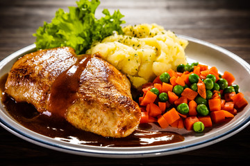 Roast chicken breast with mashed potatoes, carrot and green peas on wooden background