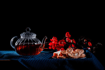 Hot tea in a glass teapot on a black background. saucer with cookies
