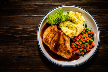 Roast chicken breast with mashed potatoes, carrot and green peas on wooden background