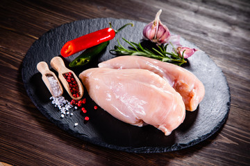 Raw chicken breasts with spices on black stone plate