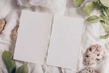 Wedding invitation mockup with paper, stone, green branch on white textile background. Top view,...
