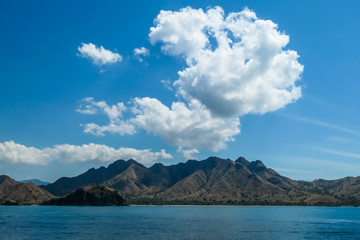 A view on idyllic island in Komodo National Park, Indonesia. There are few clouds above the island. Calm and clear surface of the sea. Island hoping. Perfect day for sailing