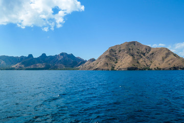 Fototapeta na wymiar A view on idyllic island in Komodo National Park, Indonesia. There are few clouds above the island. Calm and clear surface of the sea. Island hoping. Perfect day for sailing
