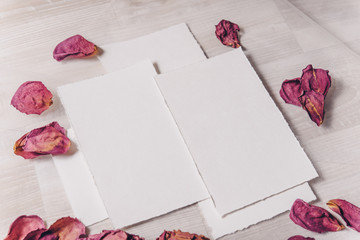 Wedding invitation mockup with paper, rose, green branch on white textile background. Top view, flat lay. Wedding stationary. Perfect for presentation of your wedding invitation, menu, greeting cards