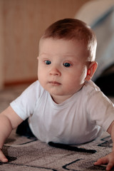 The kid is very surprised and amazed. The baby was thinking about something. The boy lies on his stomach on the floor. A little boy is playing on the floor.