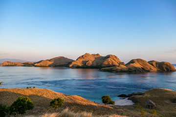 A view on a the morning sun rising over an island formation in Komodo National Park, Flores, Indonesia. Golden hour over the islands and sea. Idyllic landscape. New day beginning. Chocolate hills.