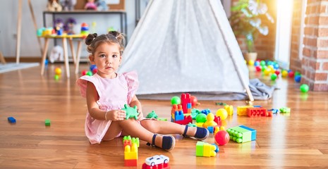 Young beautiful toddler sitting on the floor playing with building blocks at kindergaten