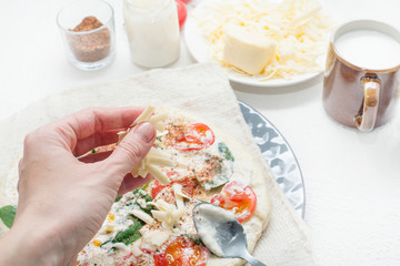 In the process of making pizza, manually pour cheese on the finished dish, against the background of the ingredients used. The concept of making pizza.