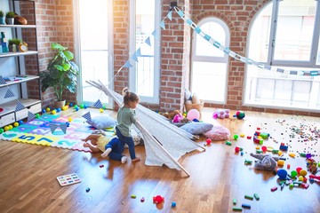 Adorable toddlers playing with tipi around lots of toys at kindergarten