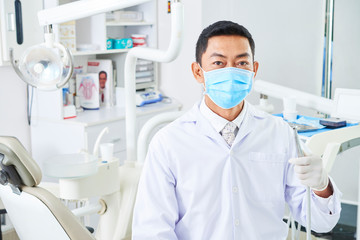 Horizontal portrait if unrecognizable Asian dentist wearing face mask holding dental drill