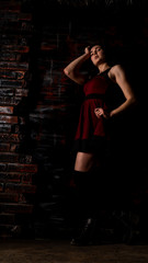 Fototapeta na wymiar Pretty young sexy model female with dark hair in amazing long red dress and black shoes posing in dark studio
