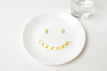 Multivitamin and fish oil capsules in a shape of smile emoji.