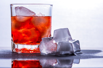 Glass of whiskey and ice on a glass table.