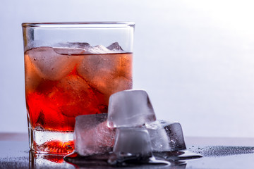 Glass of whiskey and ice on a glass table.