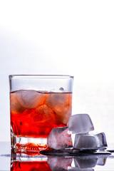 Glass of whiskey and ice on a glass table.