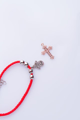 Religion attributes, red bracelete and golden cross. White background. Top view, flat lay.