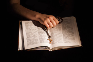Naklejka premium Female hand holding opened holy bible and crucifix. Book pages with religious text, reading word of God.