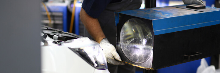 Close-up on male mechanic hands holding big replaced headlamp and making headlight ready plunge in socket of sport automobile at modern repairing service station. Blurred background © H_Ko