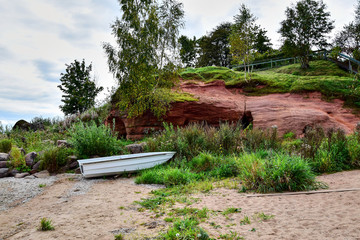 Fototapeta na wymiar Estonia, the shore of Lake Peipus, a red sandstone hill covered with green grass and trees, a sandy beach with a white boat, in the fall afternoon.