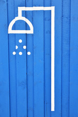 Shower sign painted in white on blue wood. Outdoors on beach.