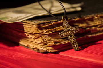 Ornamented decorative golden cross and old book close-up. Christian religion items and money.