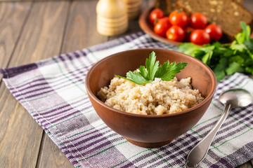 Healthy vegetarian breakfast with wheat porridge, bread, tomatoes and parsley on wooden rustic table