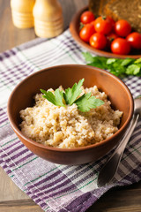 Healthy vegetarian breakfast with wheat porridge in a bowl, bread, tomatoes and parsley on wooden rustic table