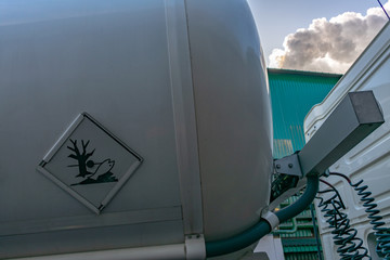Danger plate on tank truck of dangerous goods and smoke coming out of a industry