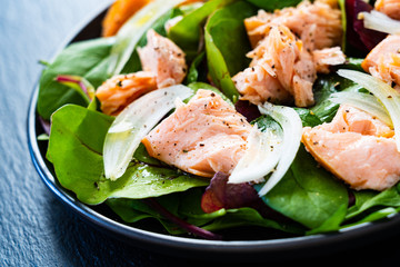 Salmon salad - roasted salmon and vegetable leaves on black stone background