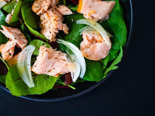 Salmon salad - roasted salmon and vegetable leaves on black stone background