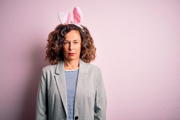 Middle age beautiful woman wearing bunny ears standing over isolated pink background skeptic and nervous, frowning upset because of problem. Negative person.