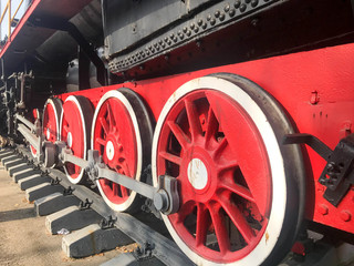 Large iron wheels of a red and black train standing on rails and suspension elements with springs of an old industrial steam locomotive
