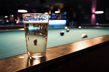 in a billiard parlor on the rail of a pool table is a glass with a beer
