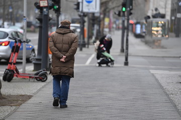 A woman with crossed hands behind the back goes for a walk on the Kuhdamm in Berlin Germany on a cold winter day.