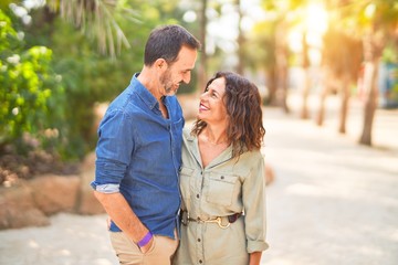 Fototapeta premium Middle age beautiful couple smiling happy and confident at town park. Standing with smile on face and hugging