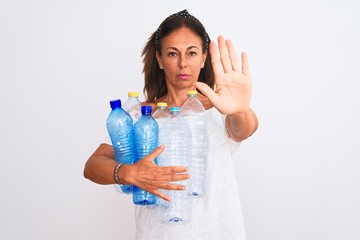 Middle age beautiful woman recycling plastic bottles standing over isolated white background with open hand doing stop sign with serious and confident expression, defense gesture