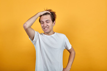 Emotional man in white t-short yellow background grimace discontent. Holding hand to hair