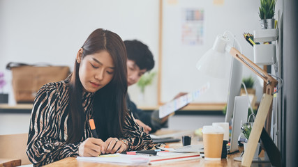 Photo of young creative designer team working/drawing/sketching a new project while sitting at the wooden working desk with the modern studio as background.