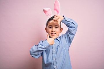 Young little boy kid wearing easter bunny ears over isolated pink background smiling making frame...