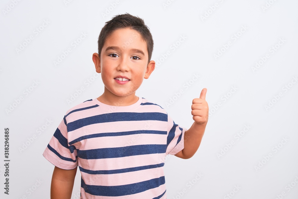 Sticker Beautiful kid boy wearing casual striped t-shirt standing over isolated white background doing happy thumbs up gesture with hand. Approving expression looking at the camera showing success.