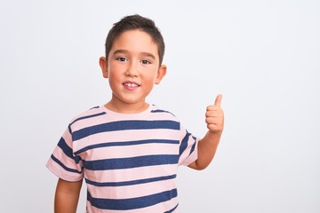 Beautiful kid boy wearing casual striped t-shirt standing over isolated white background doing happy thumbs up gesture with hand. Approving expression looking at the camera showing success.
