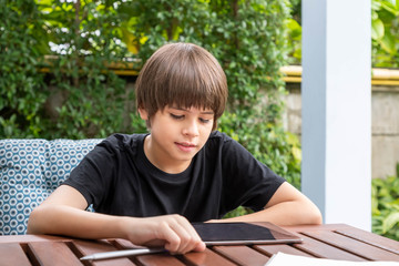 Cute boy using tablet while doing homework in garden at home
