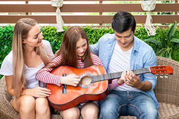 Happy family singing, and enjoy music in garden at house. Dad teaching daughter to play guitar,  family relationship concept.