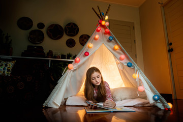 Attractive cute girl lying and reading book inside tepee tent in her bedroom enjoy happy time.