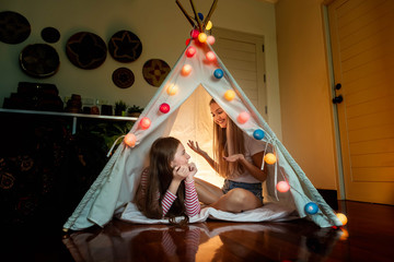 Happy mother and daughter inside tepee tent in bedroom, enjoy talking and story telling; family relationship concept.
