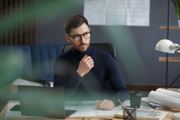 Architect working in office with laptop. Business portrait of handsome bearded man wearing eyeglasses sitting at workplace. Confident businessman became successful. Business concept.