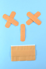 Funny smile made with brown adhesive bandages on the bright blue background