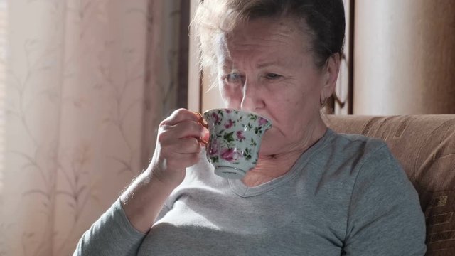Elderly woman reading a book and drinking hot coffee or tea. Comfort at home