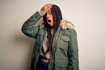 Young african american woman wearing winter parka coat over isolated background surprised with hand on head for mistake, remember error. Forgot, bad memory concept.