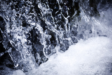Close up of waterfall stream and drops with foamy bottom on summer day background, texture and wallpaper
